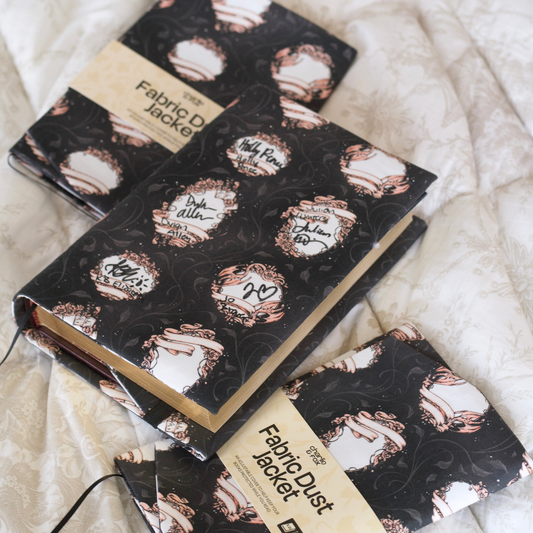 A book with a black fabric dust jacket featuring blank book plates on top of a white blanket. 