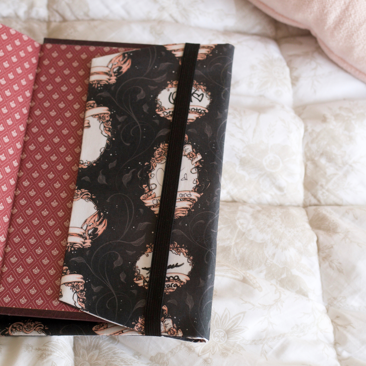 A book with it's back cover wrapped in the back flap of a black fabric dust jacket featuring blank book plates on top of a white blanket. 
