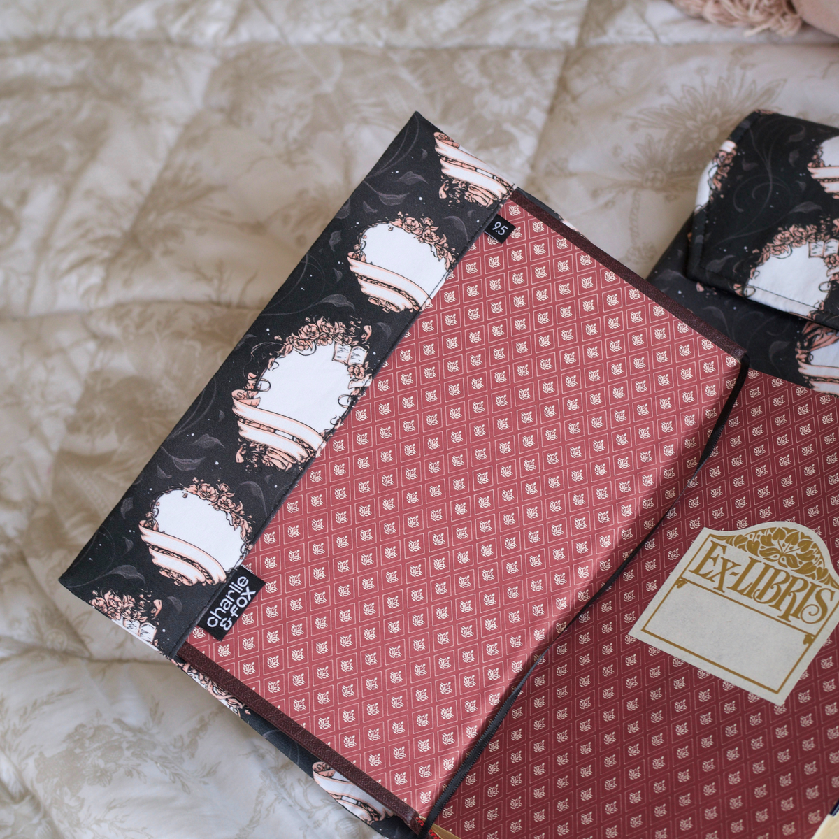 An open book with it's front cover in the front pocket of a black fabric dust jacket featuring blank book plates on top of a white blanket. 
