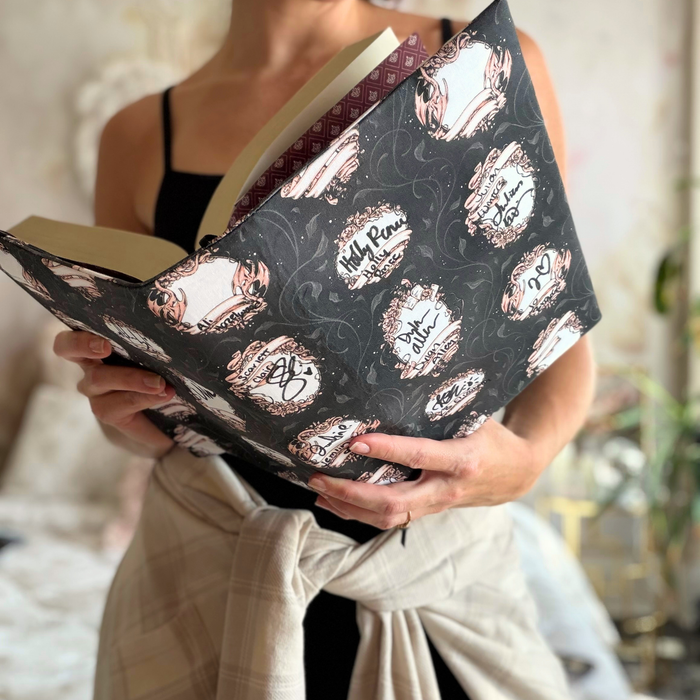 A woman holding an open book in a black fabric dust jacket featuring blank book plates against a blurred background. 